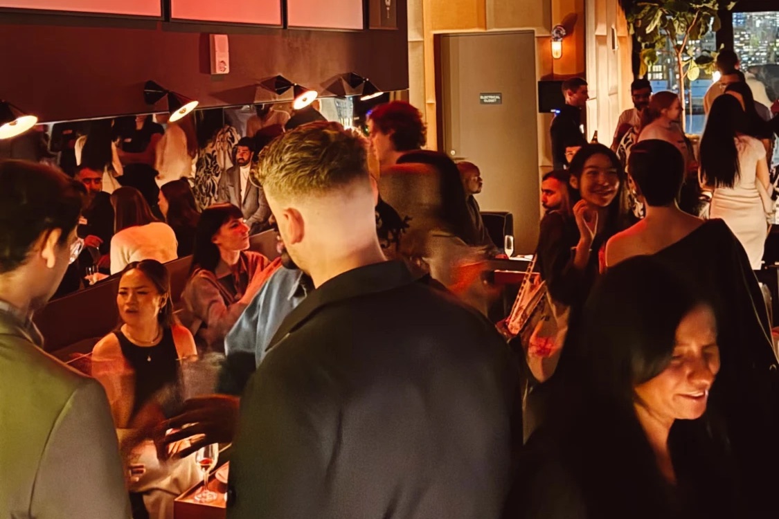 A packed room of designers talking over drinks under warm lighting