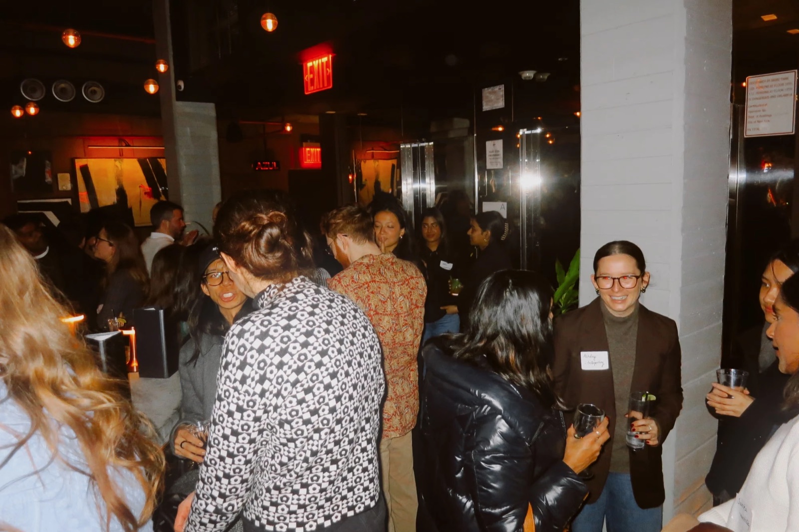 Smiling attendees wearing name tags and holding drinks mid-conversation