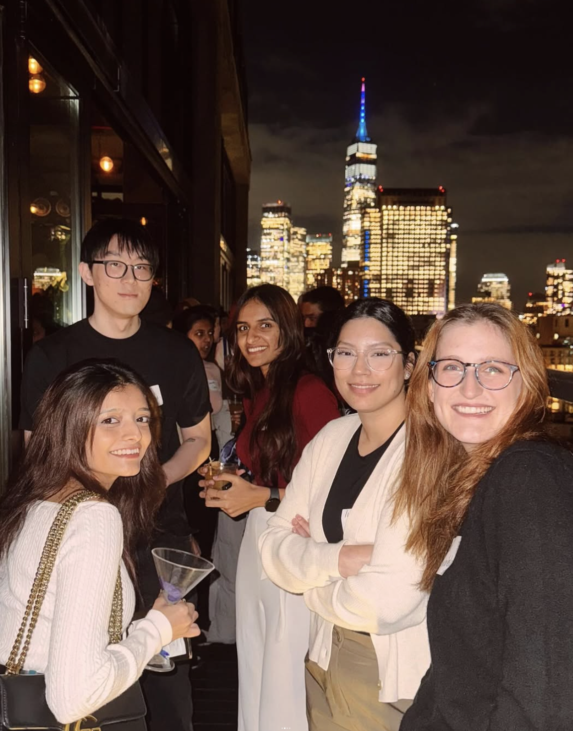 Designers with cocktails on a balcony, the lit Manhattan skyline behind them